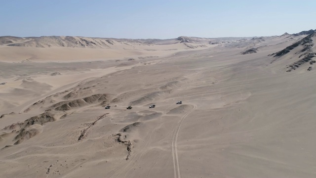 4K空中后视图的车队4x4车辆之间的沙丘和山脉之间的骨骼海岸，纳米比亚沙漠，纳米比亚视频素材