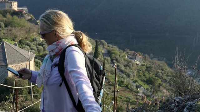 女徒步旅行者在山坡上的城堡上用智能手机聊天视频素材