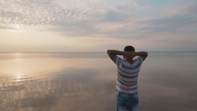 一个年轻人站在死海的岸边，欣赏美丽的日出。美丽的海景黎明。视频素材