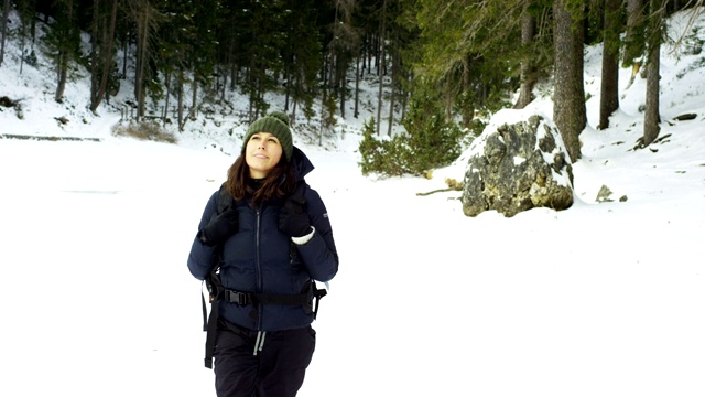 一个女孩在树林里和雪地里散步，呼吸着纯净的空气，微笑着在大自然的山上行走，背着徒步背包。视频素材