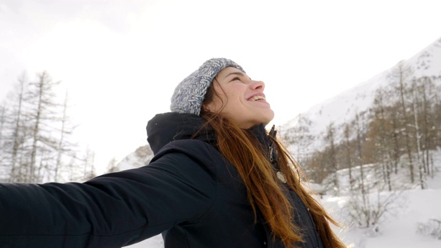 在冬天的一天，一个美丽的女人在山上玩雪，呼吸着清新的空气，沉浸在大自然中。视频素材