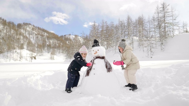 一个冬天的一天，在积着雪的山上，两个小女孩玩着玩雪人。视频素材