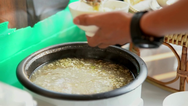 特写:男子将热粥米饭舀进碗里。视频素材