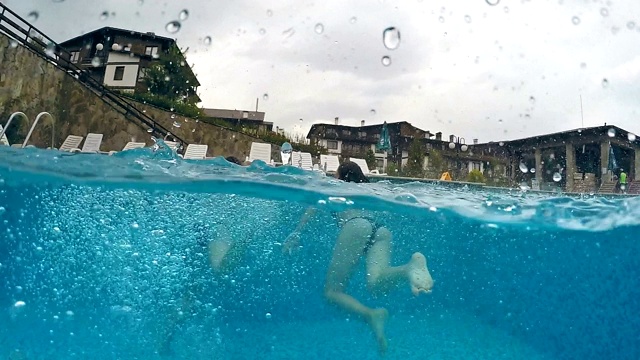 在雨天，两个女孩用腿在游泳池里戏水，gopro圆顶半水下视图，慢动作视频素材