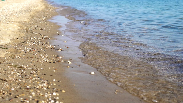 夏季概念背景，海边有平静的海浪拍打着海滩上的沙子和卵石，电影的dof视频素材