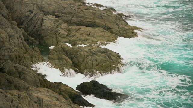 海浪冲击着多岩石的海岸。白色的浪花滴落在岩石上视频素材