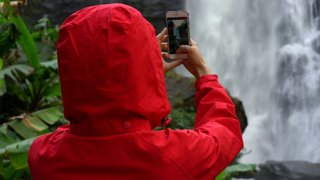 身穿红色雨衣的冒险女子拍摄瀑布照片视频素材