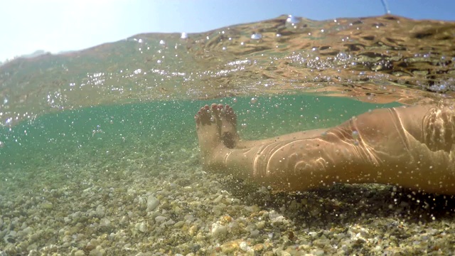 女性足部放松漂浮在浅海中，夏日度假概念，半水下观gopro圆顶拍摄视频素材