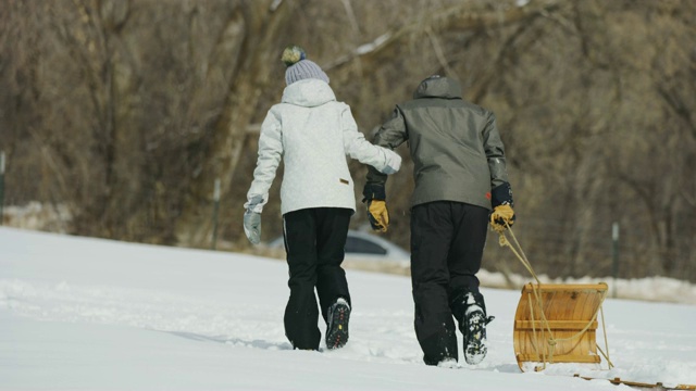 在冬季雪中拉雪橇上山的夫妇的后视图跟踪拍摄/南叉，犹他州，美国视频素材