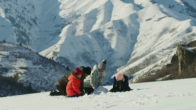 美国犹他州南福克山附近，一家人跪在雪地里堆雪人视频素材