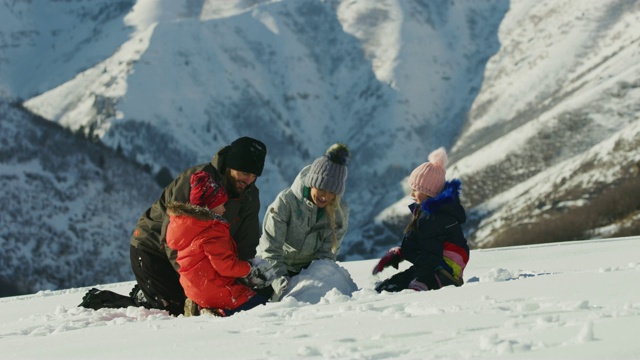 美国犹他州南福克山附近，一家人跪在雪地里堆雪人视频素材