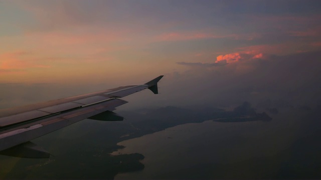 从飞机窗口座位观看旅行视频。清晨或日落的黄昏景色会降低速度和降落。用彩色的天空背景来降低飞往目的地的飞行水平。视频素材