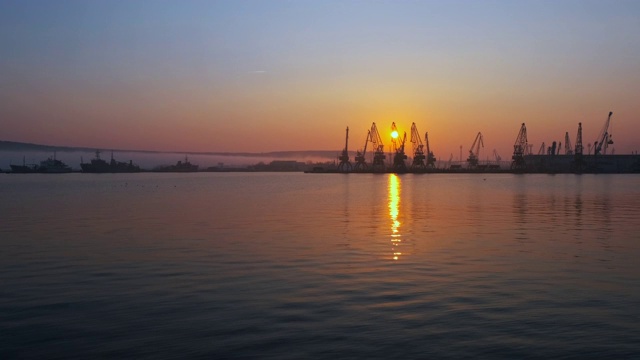 海上城市港口。海面平静扰动。一群海鸟，海鸥，在明亮的橙色夕阳的背景下，在船只和起重机上空盘旋视频素材