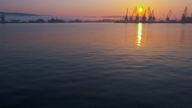 海上城市港口。海面平静扰动。一群海鸟，海鸥，在明亮的橙色夕阳的背景下，在船只和起重机上空盘旋视频素材