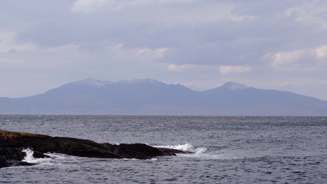 苏格兰岩石海岸上的海浪和远方朦胧的阿兰视频素材