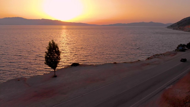 无人机:金色的夕阳照亮了海边和沿着风景优美的道路行驶的汽车。视频素材