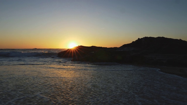 海滩上的湿沙和大西洋海浪淹没了它。太阳滑动的黑色岩石在日落葡萄牙。UHD视频素材