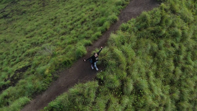 女旅行者双臂高举在山顶看风景徒步女孩举起手臂庆祝风景，享受假期旅行冒险的自然。鸟瞰图视频素材