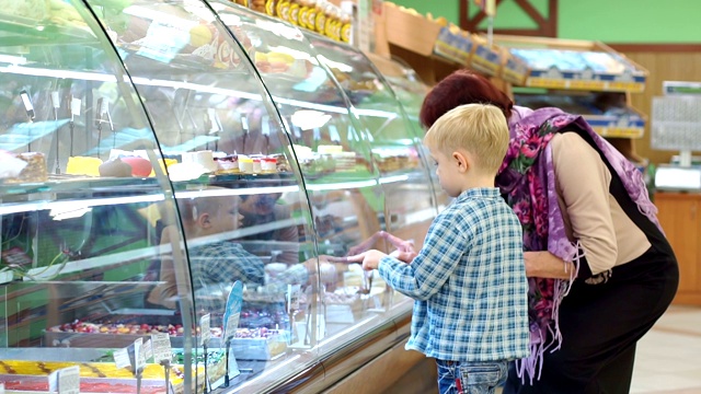 一位奶奶带着小孙子在商店的柜台上挑选糖果。视频素材