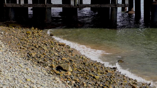 平静的海浪拍打着木板路下面的岩石海滩视频素材