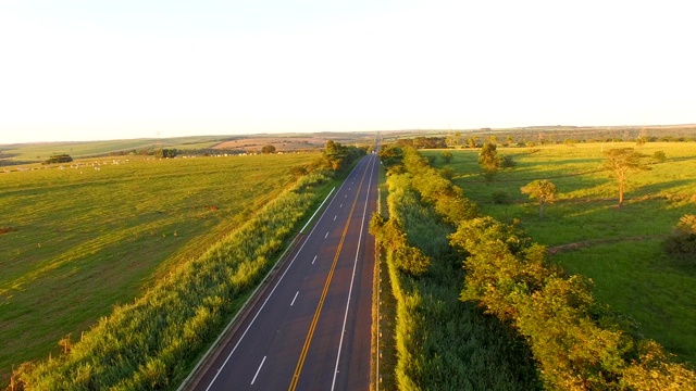 夕阳下的道路上有过往的汽车，背景是美丽的牧场视频素材