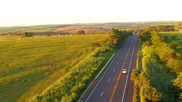 夕阳下的道路上有过往的汽车，背景是美丽的牧场视频素材