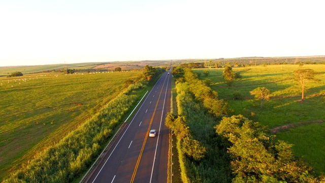 夕阳下的道路上有过往的汽车，背景是美丽的牧场视频素材