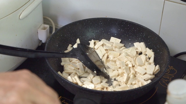 一位亚洲妇女在厨房用平底锅煎豆腐。视频素材