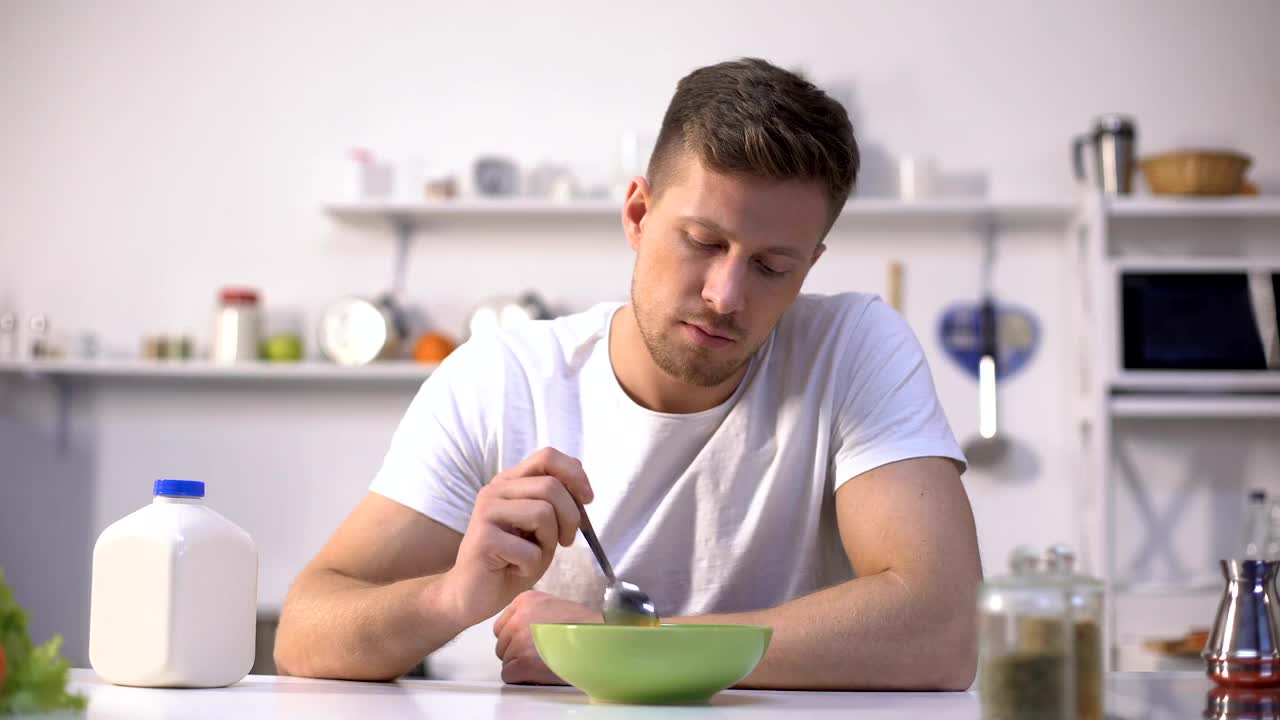 心烦的单身男子早餐吃无味的麦片，食欲不振视频素材