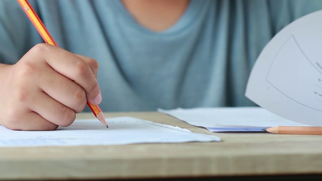 教育考试在大学或高中的概念:手持铅笔的学生测试试卷上的答案，在校园教室填写试卷。知识学习的概念视频素材