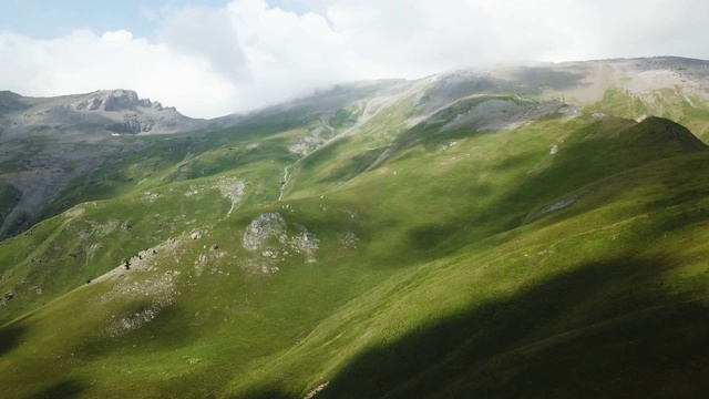 鸟瞰图。飞过绿草嶙峋的山丘。在美丽的云中飞过高山视频素材