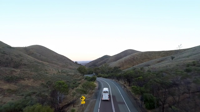 空中向前:白色巴士行驶在被土山包围的道路上——澳大利亚的乌卢鲁视频素材