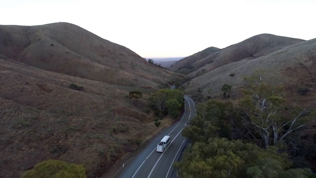 空中向前/向下:白色巴士行驶在被土山包围的道路上——澳大利亚的乌卢鲁视频素材