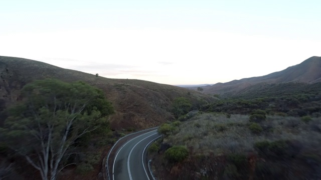 空中向前:白色巴士在灌木丛覆盖的山丘之间的道路上行驶-澳大利亚的乌卢鲁视频素材