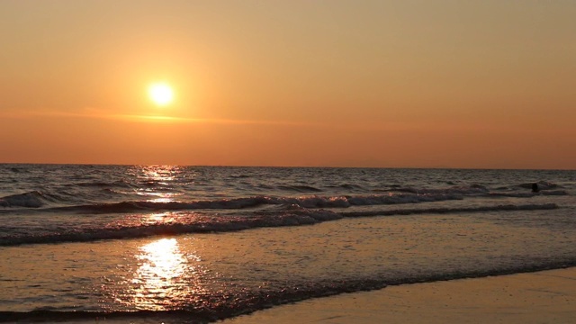 海滩上的海浪与天空的橙色光和太阳落在海上视频素材