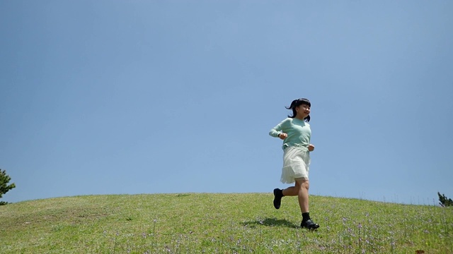 一个日本女孩在蓝天下跑下山坡视频素材