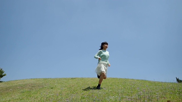 一个日本女孩在蓝天下跑下山坡视频下载