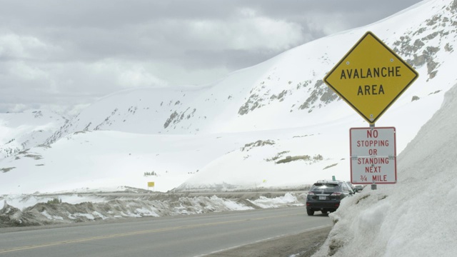 汽车沿着Loveland Pass在大陆分水岭过去一个“雪崩地区”和“禁止停止或站下3/4英里”警告路标在科罗拉多州的落基山脉下阴天在冬天视频素材