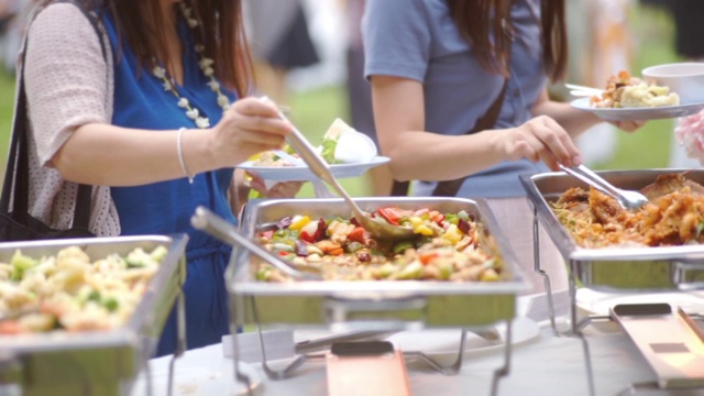 户外聚会时，人们在自助餐桌上端着盛有肉的盘子。视频素材