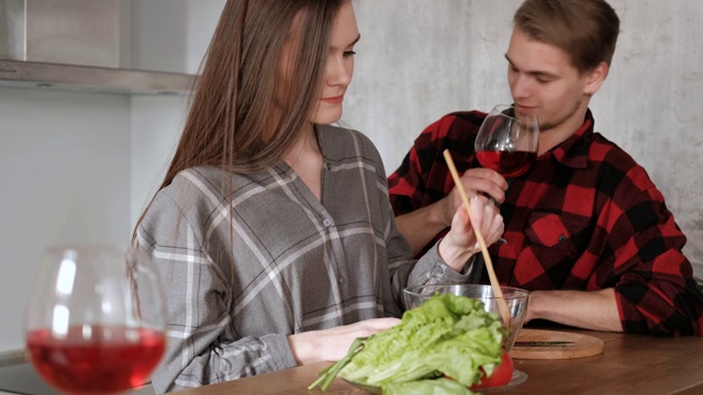 一对穿着格子衬衫的年轻漂亮夫妇正在厨房里做饭。一个女人和一个男人切蔬菜，在一个透明的玻璃盘子里用胡椒、番茄和萝卜做沙拉。视频素材