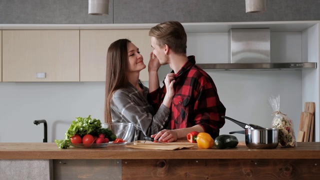 一对穿着格子衬衫的年轻漂亮夫妇正在厨房里做饭。一个女人和一个男人切蔬菜，在一个透明的玻璃盘子里用胡椒、番茄和萝卜做沙拉。视频素材