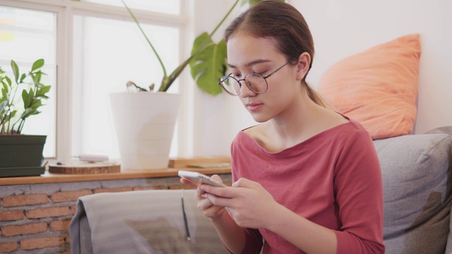 戴眼镜的年轻女子在客厅里用手机。视频素材