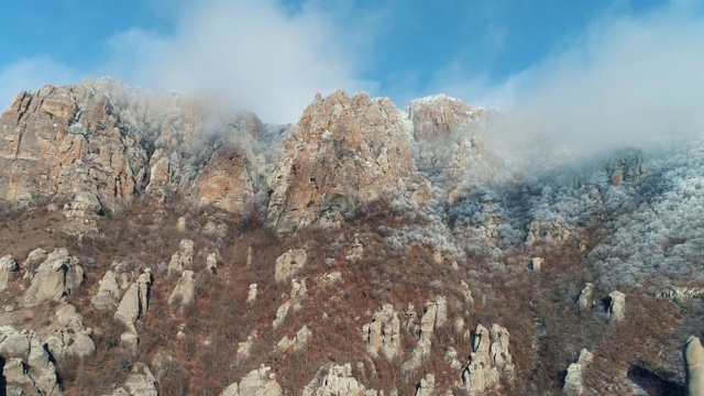 在阳光明媚的日子里，被巨大的岩石和灌木覆盖的雪山峭壁映衬着美丽的蓝天。美妙的山景视频素材