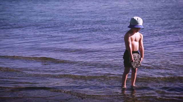 一个小男孩把一小块混凝土扔进水中，然后捡起来再做一次。暑假夏令营好玩。视频下载