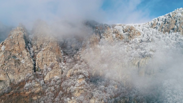 冬季景观与雪山悬崖覆盖冻结的针叶树和灌木在灰色的云对蓝色的天空。美丽的景色视频素材