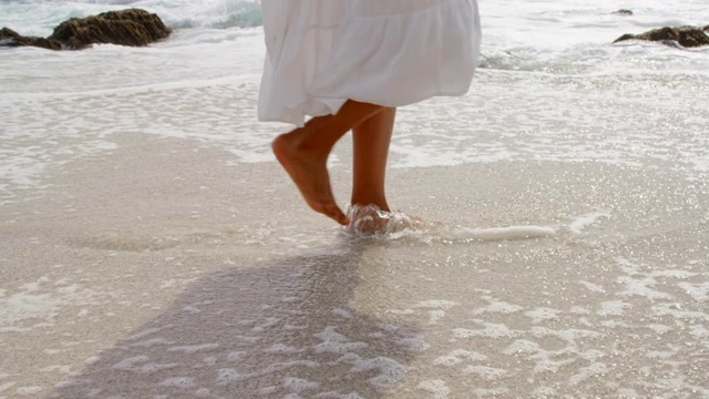 在一个阳光明媚的日子里在4k海滩赤脚行走的女人的低部分视频素材