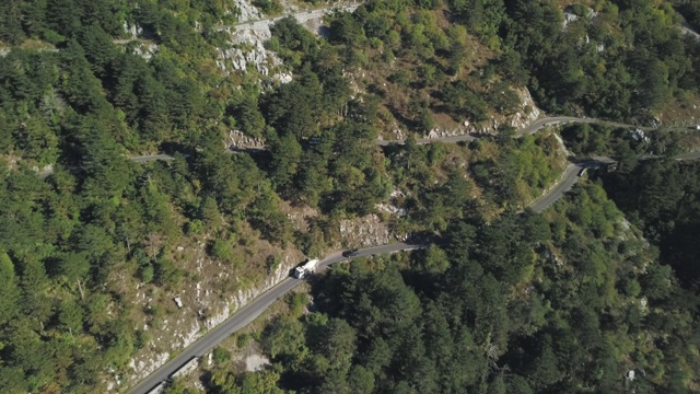 鸟瞰图山形蜿蜒的道路与卡车和汽车。股票。道路交通蜿蜒在高山狭窄的角落，汽车变成绿色的森林视频素材