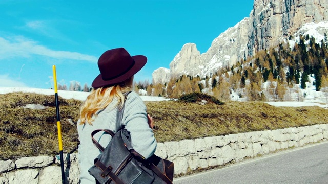 带着帽子和背包的女孩旅行者走在山间的柏油路上。视频素材