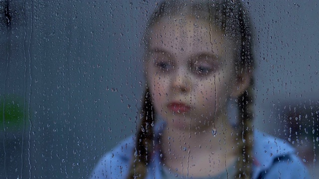 心烦意乱的女孩望着窗外的雨，忍受着孤独，等待着父母视频素材