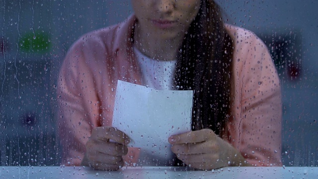 沮丧的女士抱着被撕的照片靠近雨窗，遭受痛苦的离婚视频素材